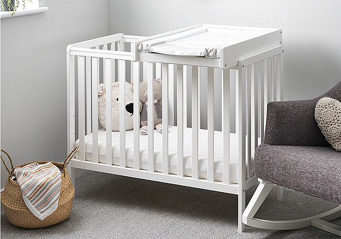 White wooden cot with cot top baby changer. Compact design, open slatted sides, teething rails.