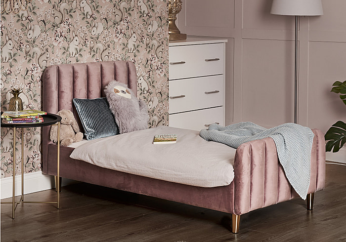 A luxurious pink velvet toddler bed frame with a deep padded headboard and footboard. Tapered gold legs.
