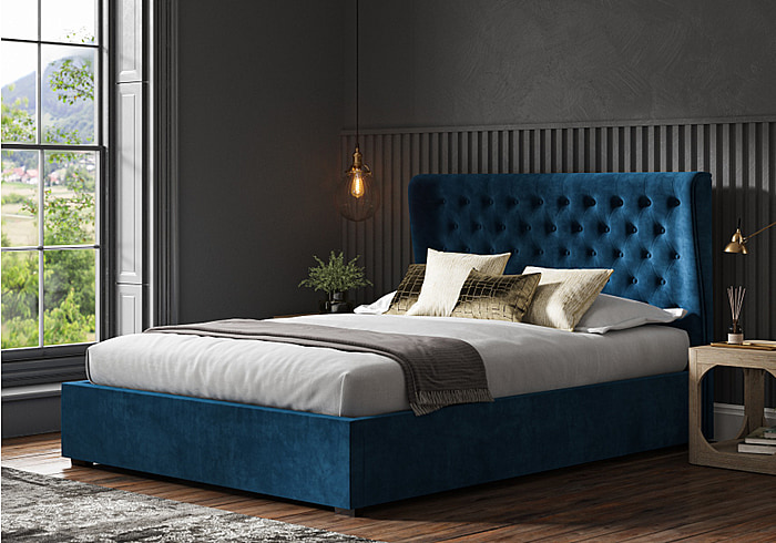 Luxurious blue velvet ottoman bed with a winged buttoned headboard and a low foot end