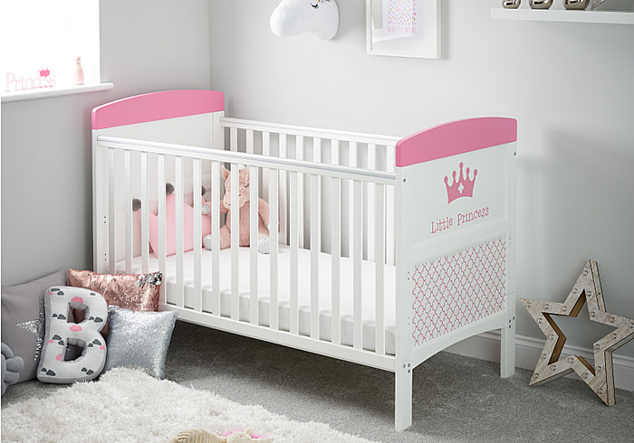 White cot bed with a royal themed design in pink, teething rails, 3 height adjustable base