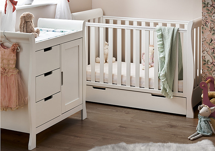 White mini cot bed and changing unit in a beautiful sleigh design. 3 position base height, teething rail and drawer.