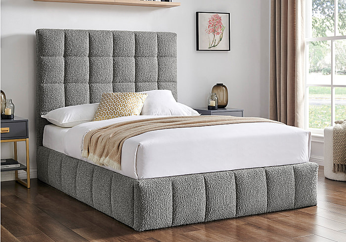 A contemporary styled ottoman bed frame with a tall square stitched headboard, upholstered in a luxury grey boucle fabric.