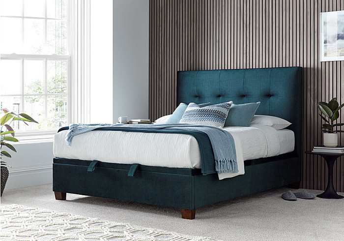 Luxurious deep blue velvet ottoman bed frame with modern dark wooden feet.