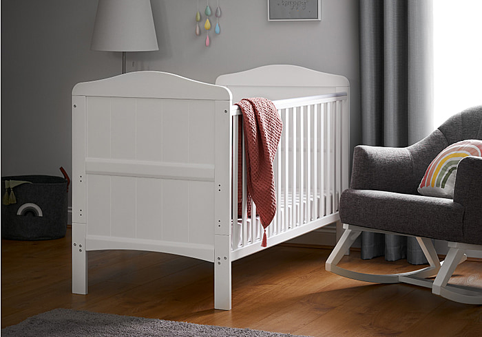 Beautiful coastal themed white wooden cot bed with grooved end panels with gentle curves. Includes teething rails.